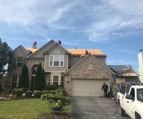 front of a single family home with a brick facade and several workers on the roof